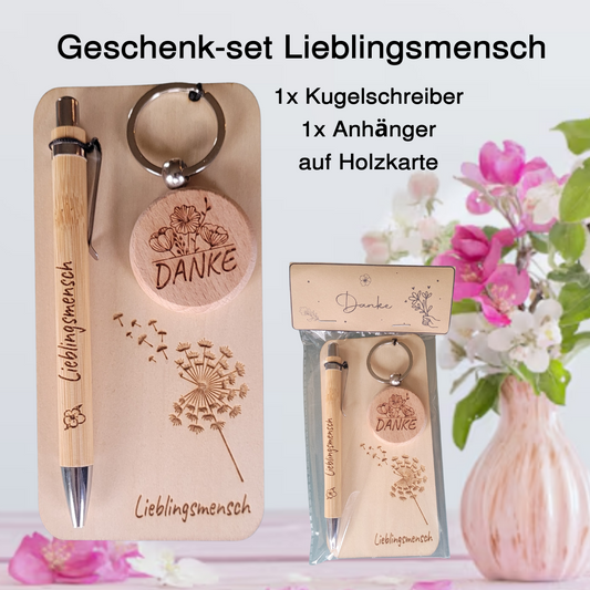 Geschenkset aus Holz: gravierter Bambus-Kugelschreiber mit Schriftzug Lieblingsmensch und runder Holz-Schlüsselanhänger mit Gravur Danke, dekorativ auf Holzplatte arrangiert.